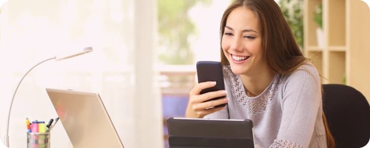 women checking her phone while working on her laptop and tablet