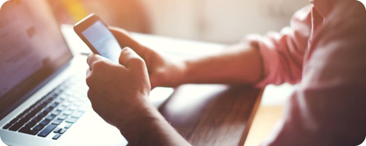 man using his phone while working on his laptop