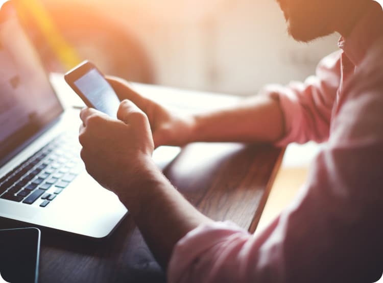 man using his phone while working on his laptop